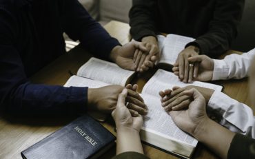 Christian Family prayer and worship. Christian group of people holding hands and praying worships to believe and Bible on a wooden table prayer meeting concept. Church Community pray together